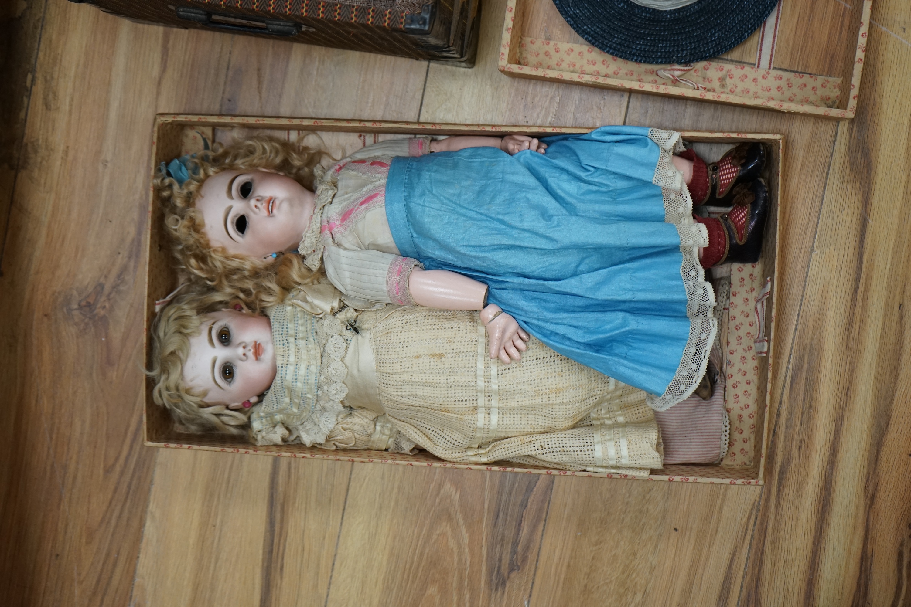 A Tête Jumeau bisque doll, closed mouth and paperweight eyes, jointed wood and composition body, two other French bisque dolls and assorted clothing, all contained within a three-layer wood and metal-bound cabin trunk, J